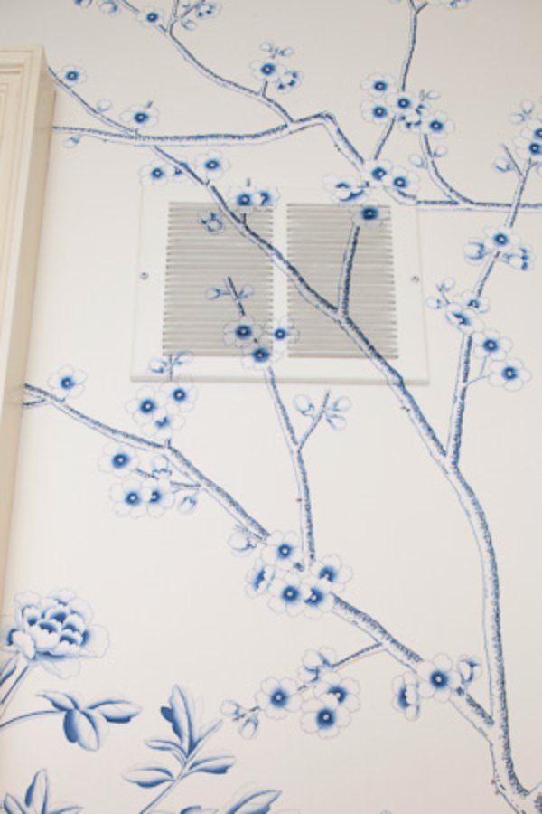 Blue blossom branches of a hand-painted mural carried seamlessly across a wall vent