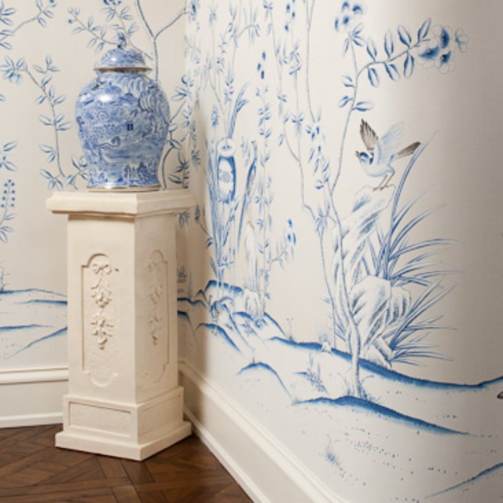 Blue hand-painted mural turning a corner behind a porcelain urn on a carved plinth