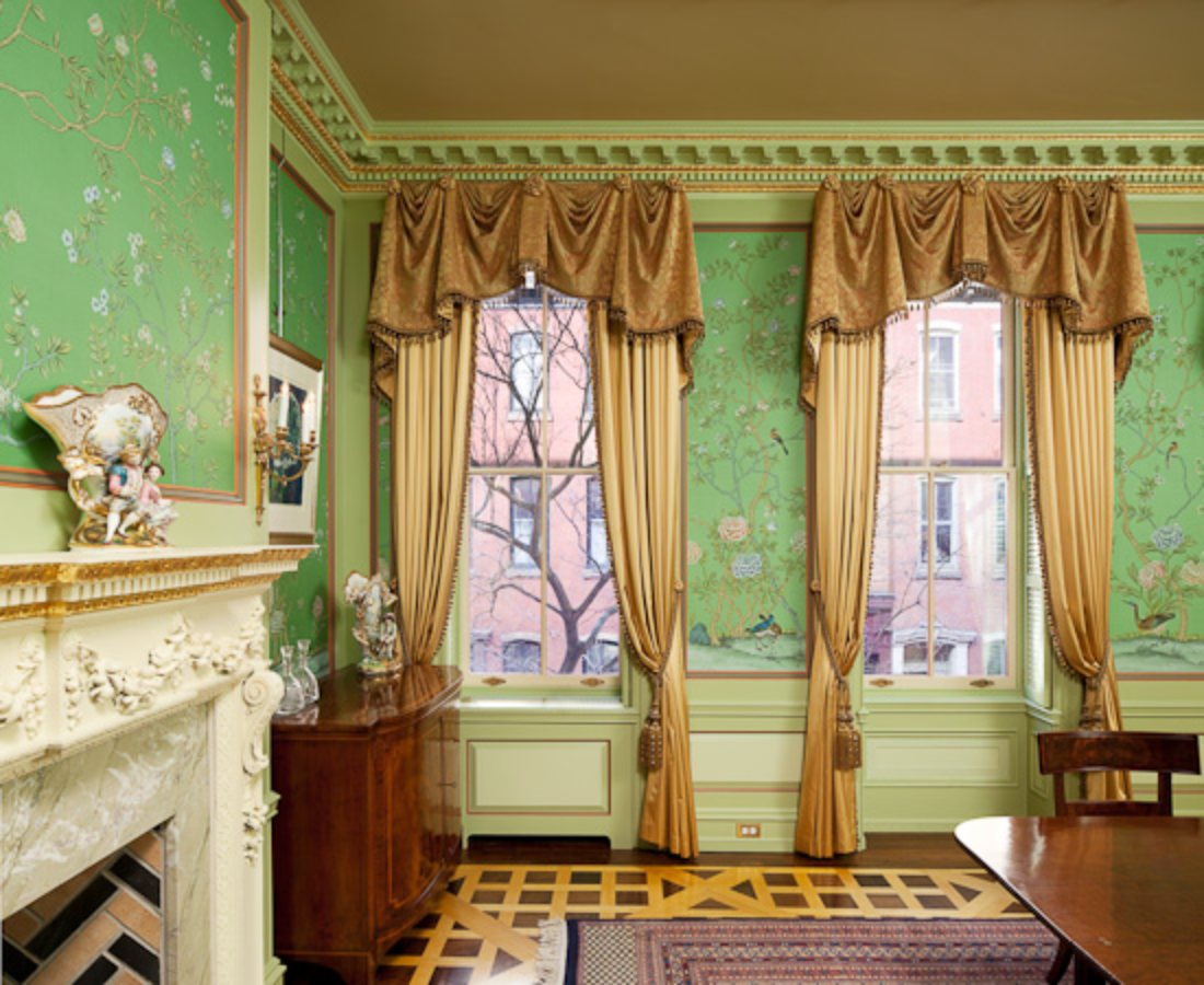 Green silk mural panels between tall windows dressed in gold drapery