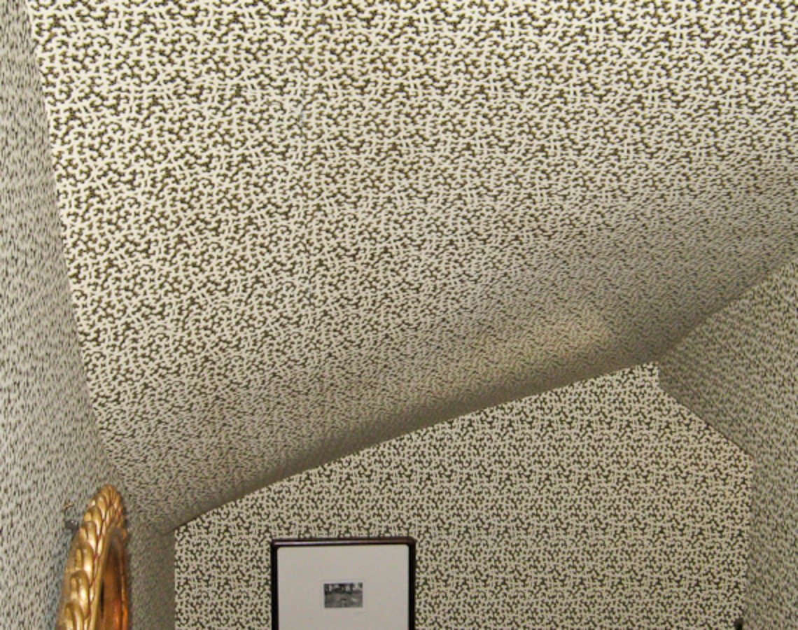 Small-scale patterned wallpaper continuing from wall onto a sloped ceiling