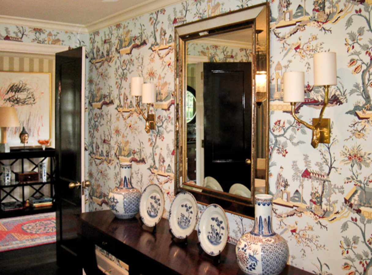 Chinoiserie wallpaper behind a gilt mirror and blue and white porcelain on a dark console