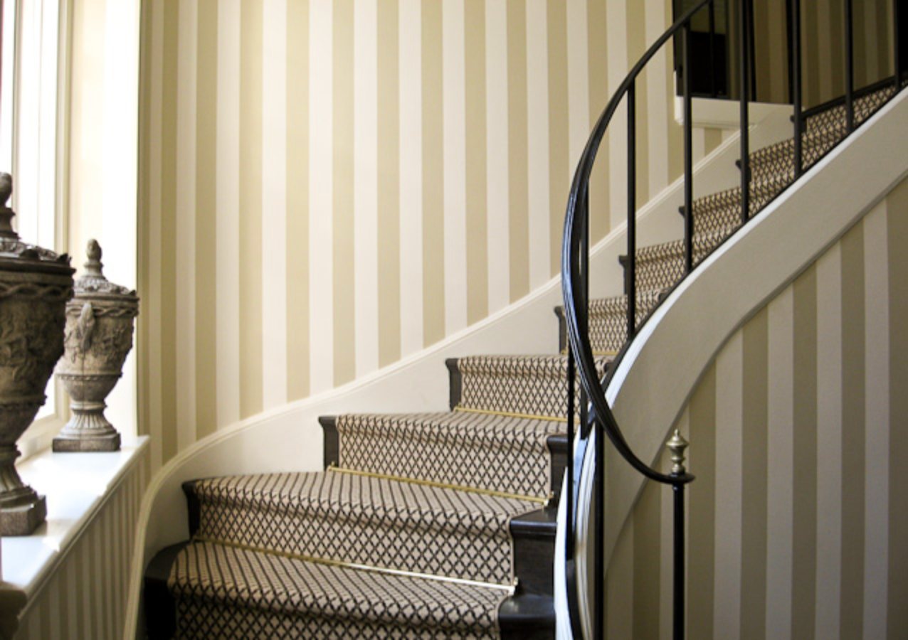 Cream and taupe striped wallpaper following a curved staircase with iron railing